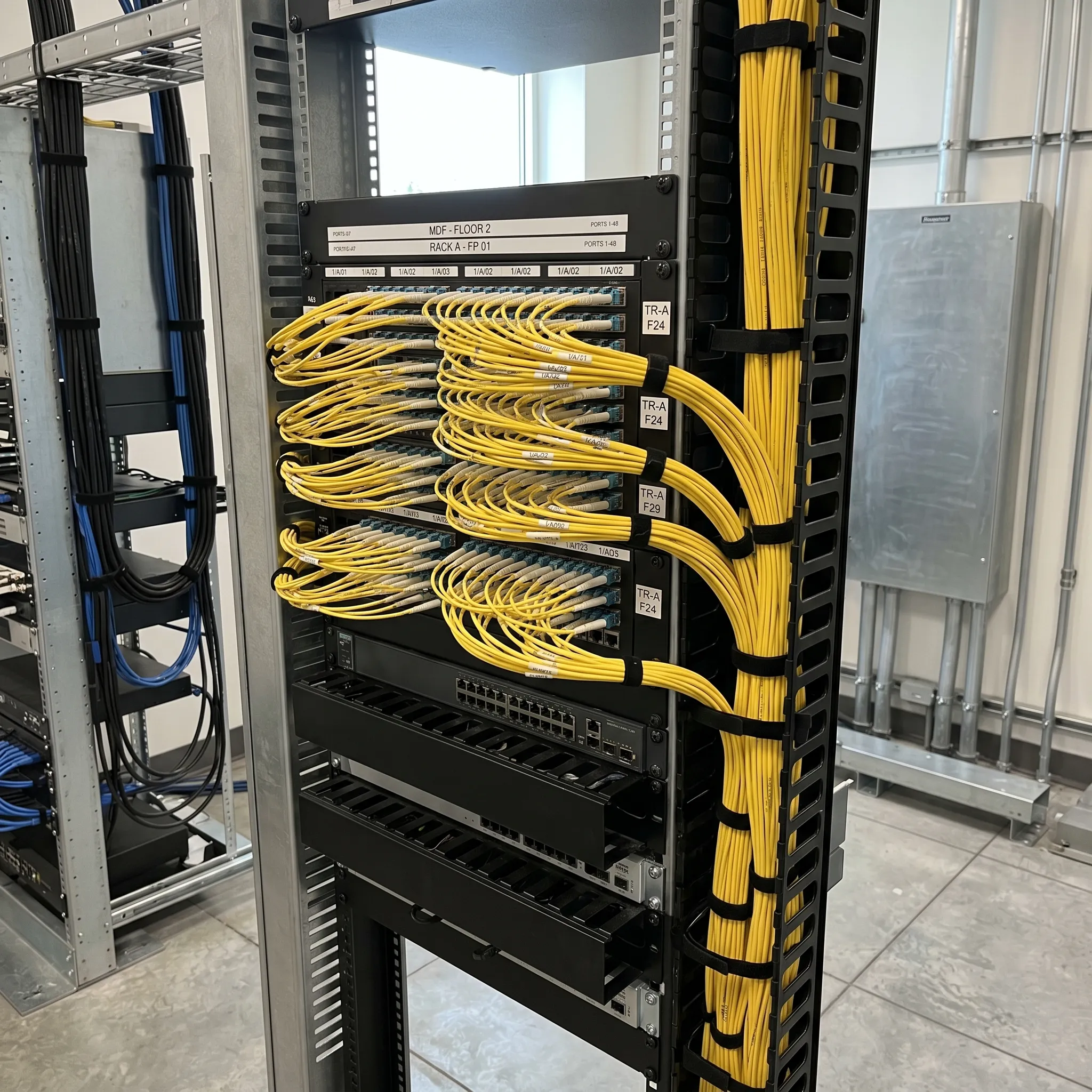 Fiber optic backbone cabling installation in commercial telecommunications room with organized patch panels and cable management